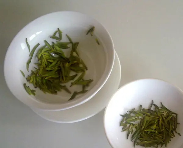 Dried green tea leaves in small white bowls